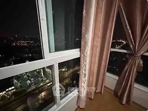 Stunning night city view from high-rise apartment window with elegant curtains.