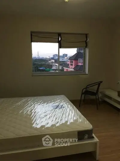 Cozy bedroom with large window offering city view, featuring a bed and chair, perfect for relaxation.