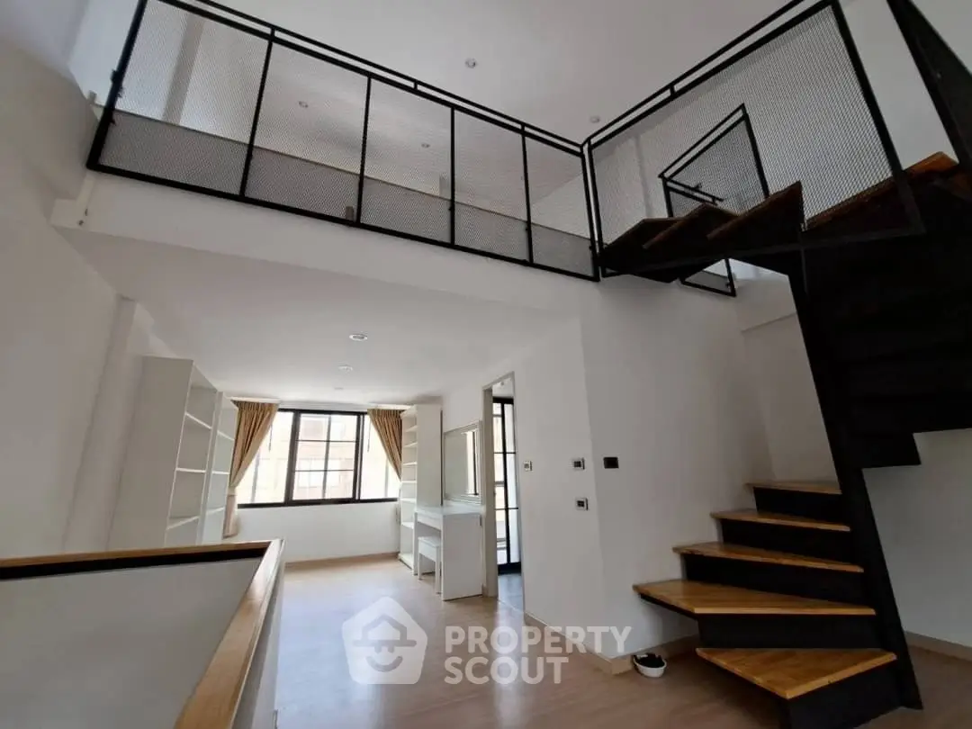Modern loft-style apartment with mezzanine and sleek staircase, featuring large windows and open layout.