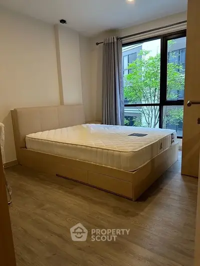 Modern bedroom with large window and wooden flooring in a stylish apartment.