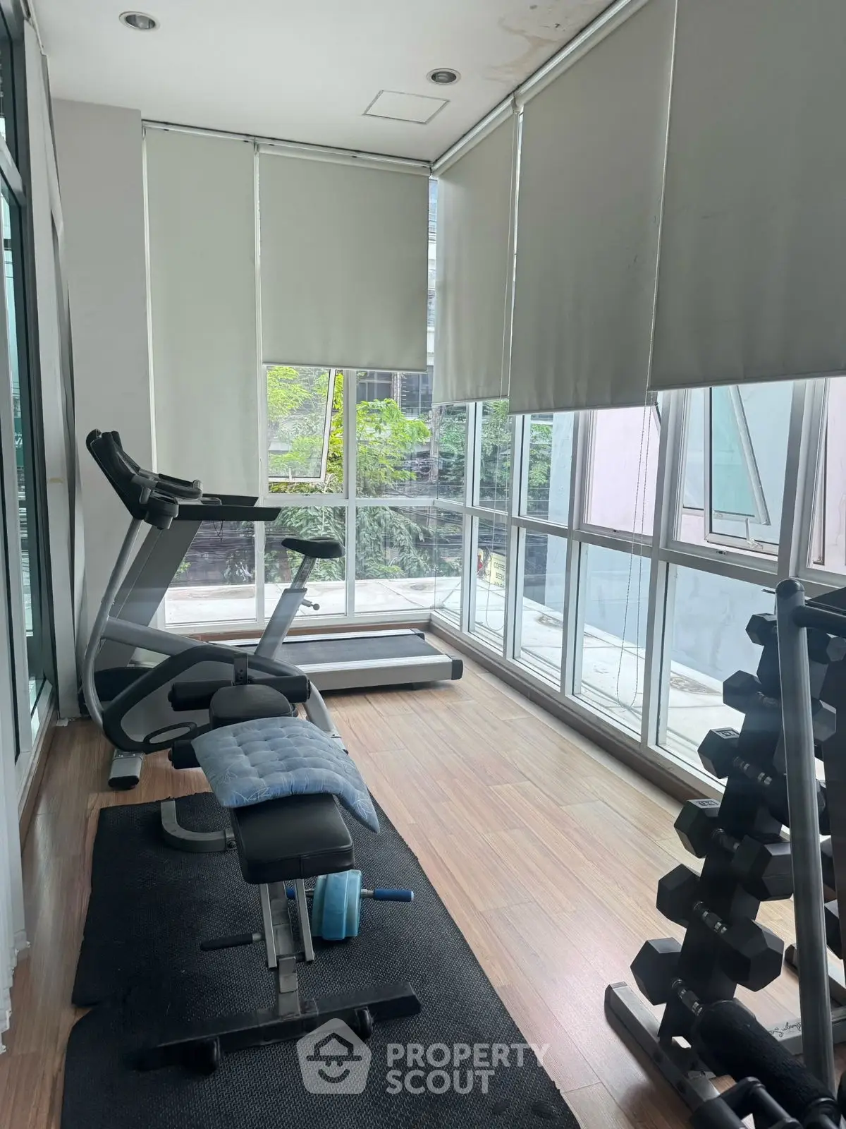 Modern home gym with treadmill and weights in bright room with large windows