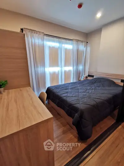 Cozy bedroom with wooden furniture and natural light through large windows.