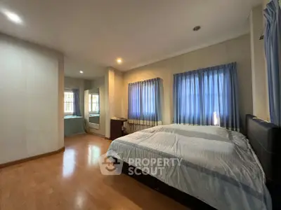 Spacious bedroom with wooden flooring and blue curtains, ideal for relaxation.