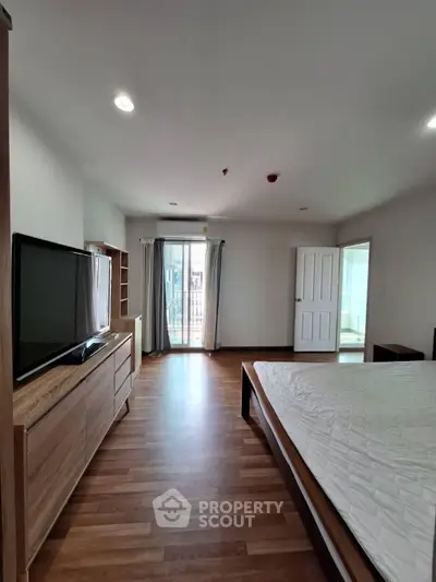 Spacious bedroom with wooden flooring and balcony access in modern apartment