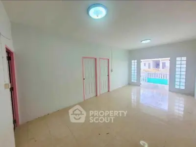 Spacious living room with tiled flooring and bright lighting, featuring large windows and pink door frames.