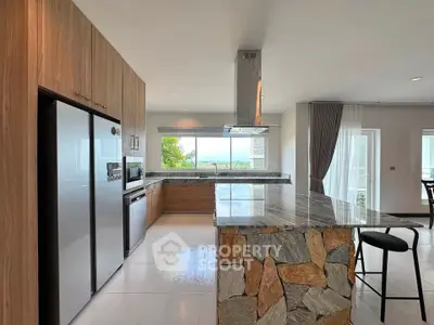 Modern kitchen with stone island and open layout, featuring large windows and sleek appliances.