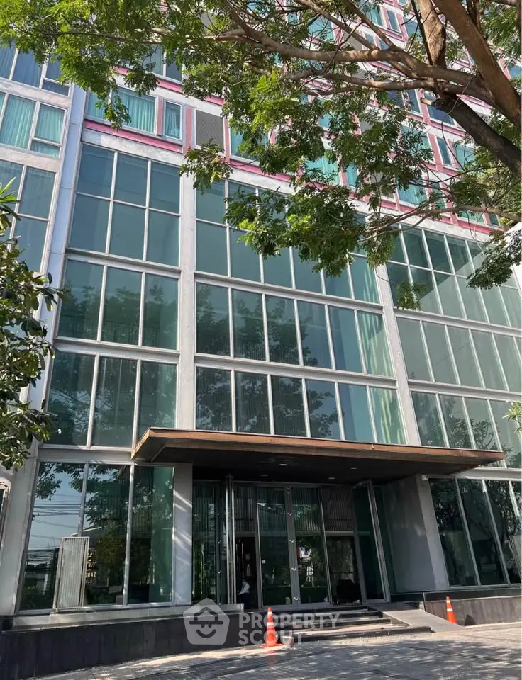 Modern glass facade of a commercial building with lush trees and sleek entrance.