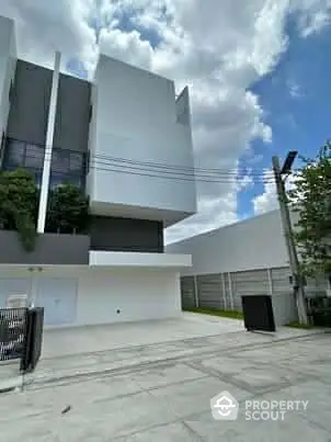 Modern architectural building exterior with sleek design and spacious driveway under a cloudy sky.