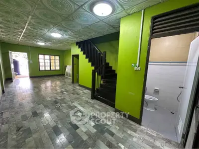 Spacious interior with vibrant green walls and unique ceiling tiles, featuring a staircase and adjacent bathroom.