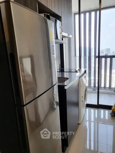 Modern kitchen with stainless steel fridge and washing machine, city view from window.