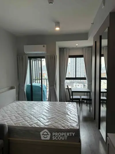 Modern bedroom with city view and balcony access in high-rise apartment.