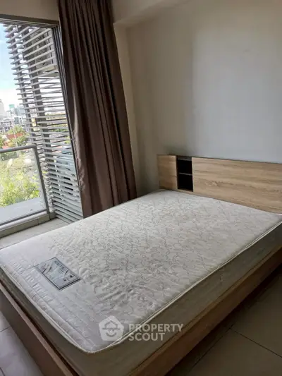 Spacious bedroom with large window and modern bed frame, offering natural light and city views.