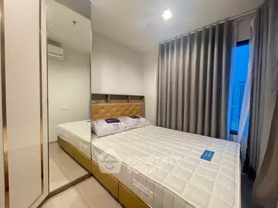 Modern bedroom with large mirror and city view, featuring elegant decor and ample natural light.