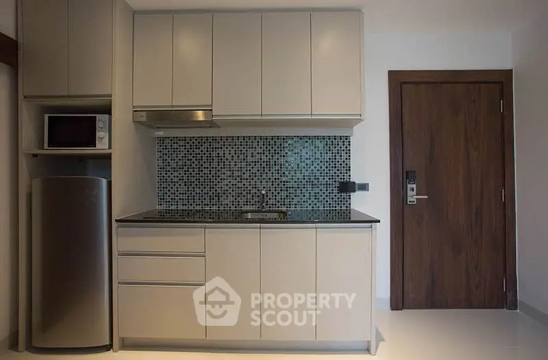 Modern compact kitchen with sleek cabinetry and mosaic backsplash in stylish apartment.