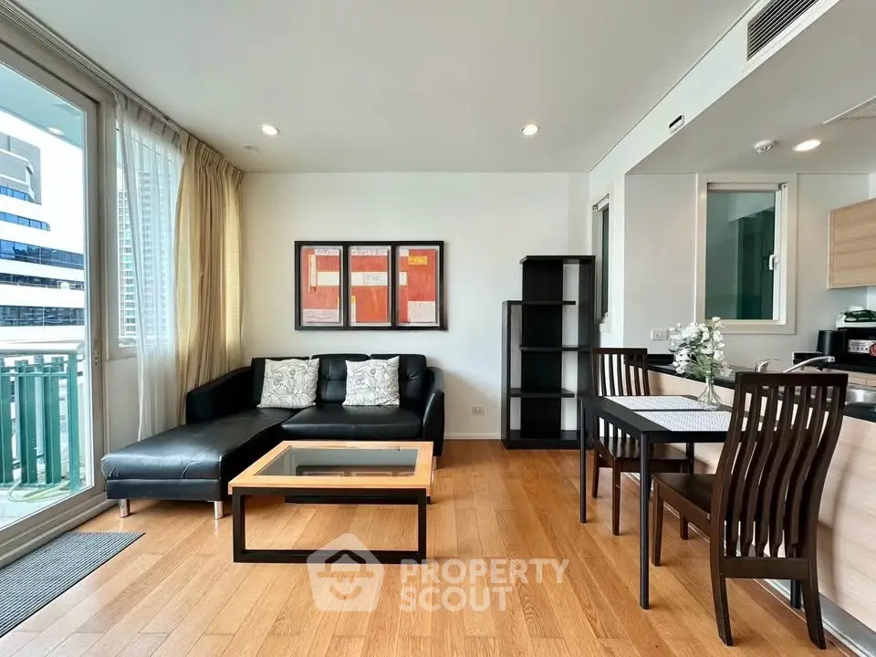 Modern living room with sleek black sofa, dining area, and wooden flooring in a high-rise apartment.