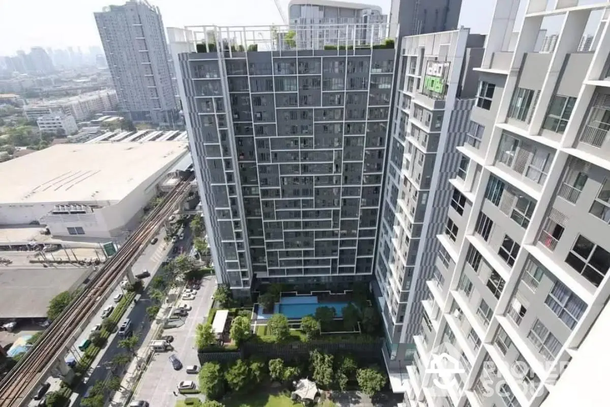 Stunning aerial view of modern high-rise building with lush garden and pool in vibrant urban setting.