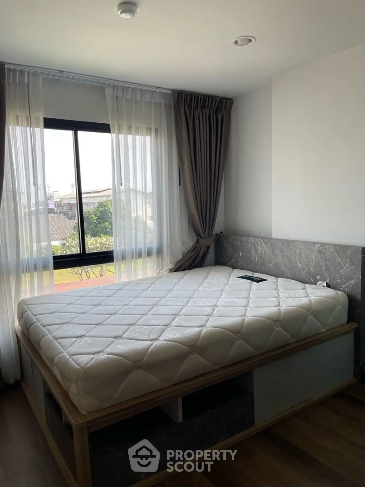 Modern bedroom with large window and stylish bed frame, offering natural light and cozy ambiance.