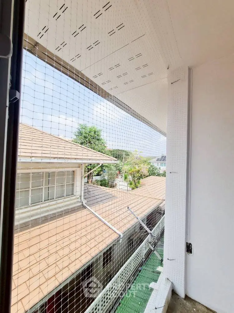Charming balcony view with safety netting overlooking neighboring rooftops and greenery.
