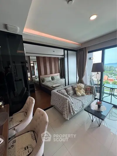 Modern condo interior with cozy living area and bedroom, featuring large windows and balcony with scenic view.