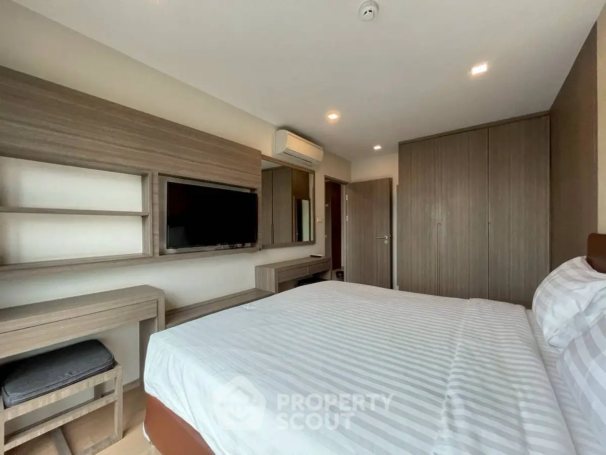 Modern bedroom with built-in wardrobe and wall-mounted TV in stylish apartment.