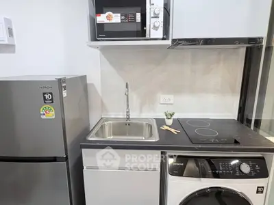 Modern kitchen with sleek appliances including fridge, microwave, and washing machine in compact layout.