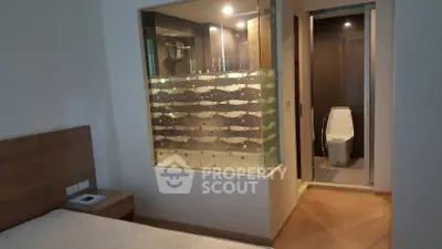 Modern bedroom with glass partition and ensuite bathroom featuring sleek design.