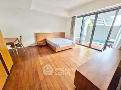 Spacious bedroom with wooden flooring and poolside balcony access