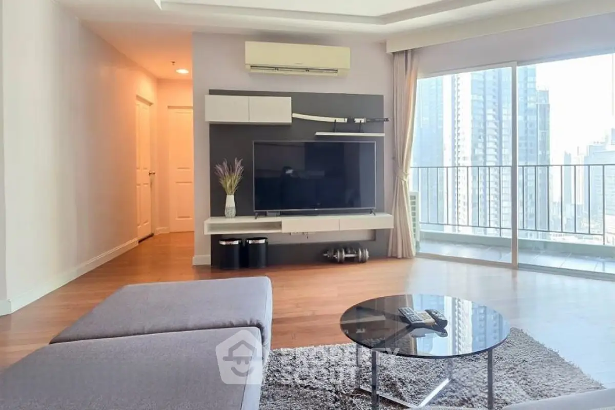 Spacious modern living room with large windows and city view, featuring sleek furniture and wooden flooring.