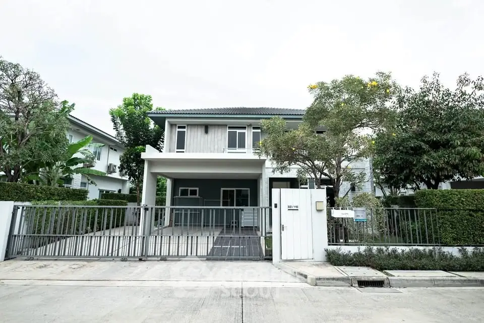 Modern two-story house with gated entrance and lush greenery