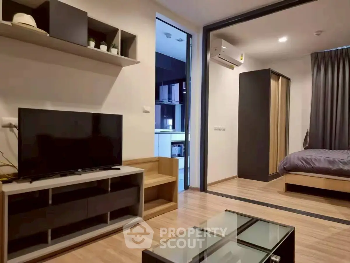 Modern living room with TV, open layout to bedroom, and sleek wooden flooring.