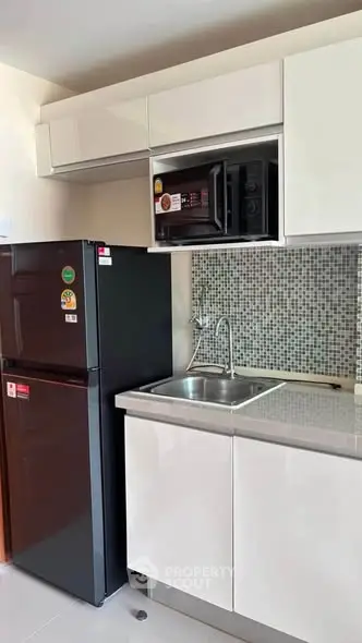 Modern kitchen with sleek cabinets, fridge, and microwave in compact layout.