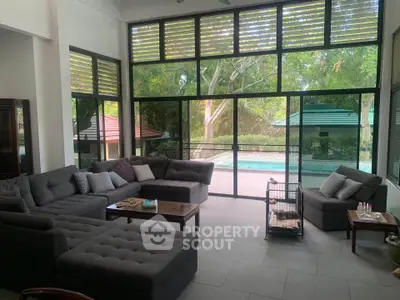 Spacious living room with large windows overlooking a serene pool and lush greenery.
