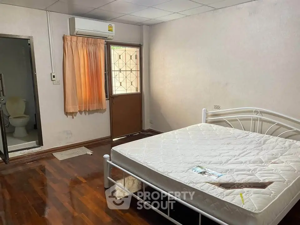 Cozy bedroom with wooden floors and attached bathroom, featuring a comfortable bed and air conditioning.