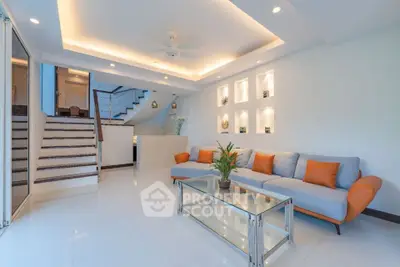 Modern living room with stylish sofa and glass coffee table, elegant lighting and staircase.