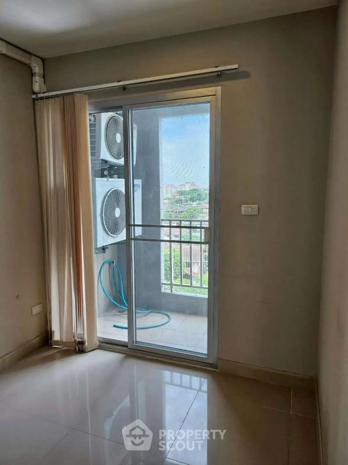 Bright room with sliding glass door leading to a small balcony with city view and air conditioning unit.