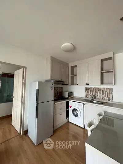 Modern kitchen with washing machine, fridge, and stylish cabinetry in a cozy apartment setting.