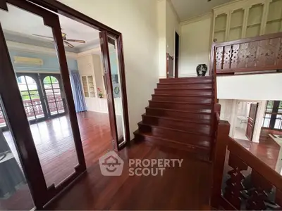 Elegant wooden staircase leading to spacious living area with large windows and natural light.