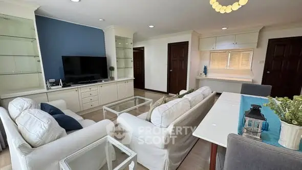 Spacious living room with elegant white sofas, glass coffee table, and built-in shelving, perfect for modern living.