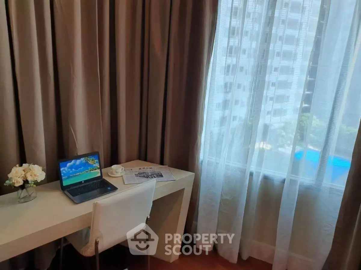 Modern study area with desk, laptop, and city view through large window.