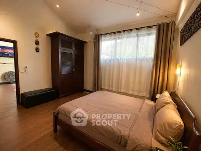 Spacious bedroom with wooden flooring and large window for natural light