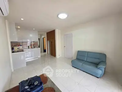 Spacious living room with modern kitchen in open layout, featuring sleek white cabinetry and cozy blue sofa.