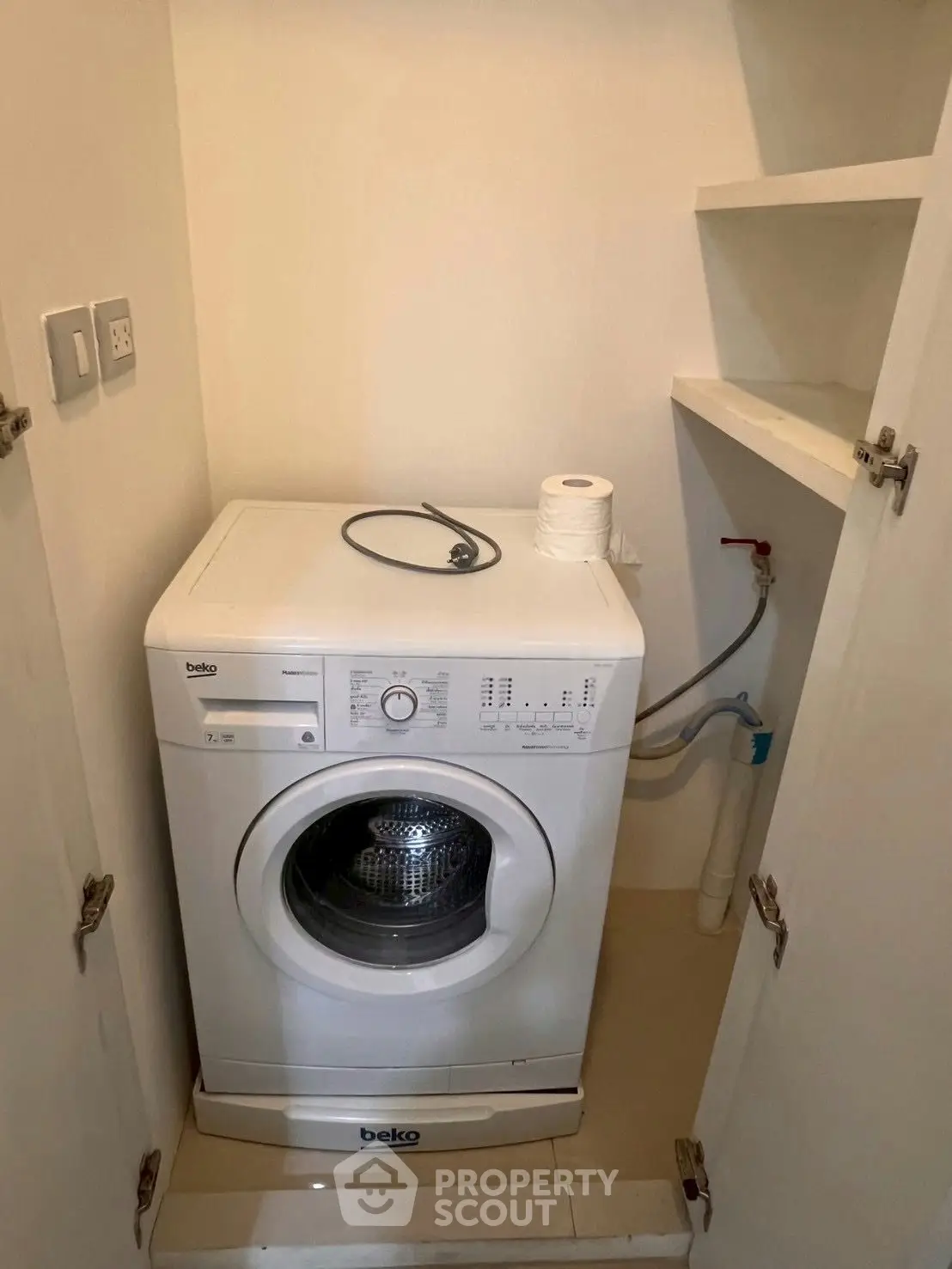 Compact laundry area with washing machine and storage shelves in modern home.