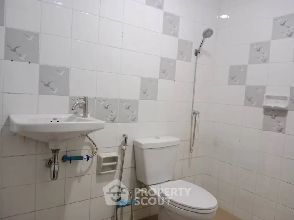 Modern bathroom with white tiles, shower, sink, and toilet in a minimalist design.