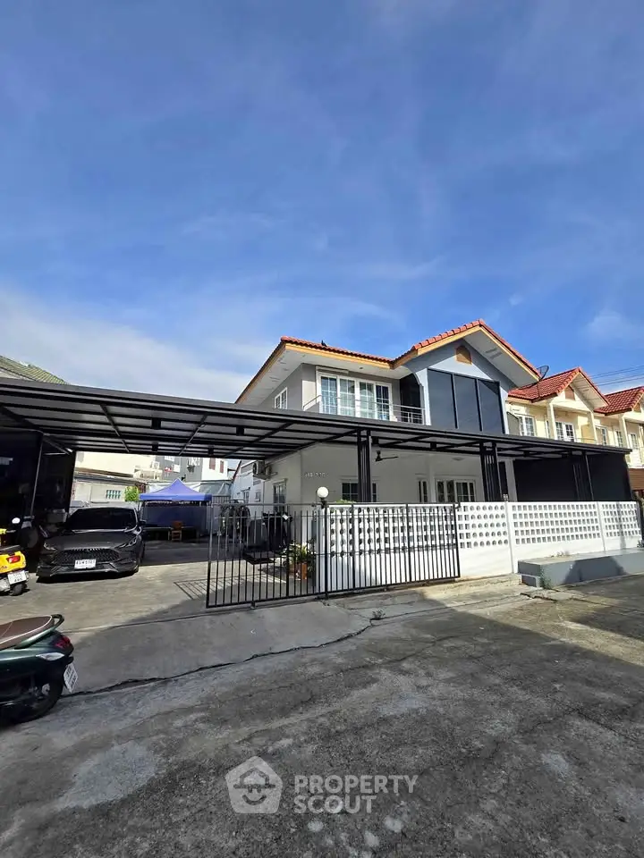 Charming two-story house with modern carport and spacious driveway under clear blue skies.