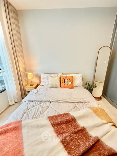 Cozy bedroom with stylish decor and natural light, featuring a comfortable bed and elegant mirror.