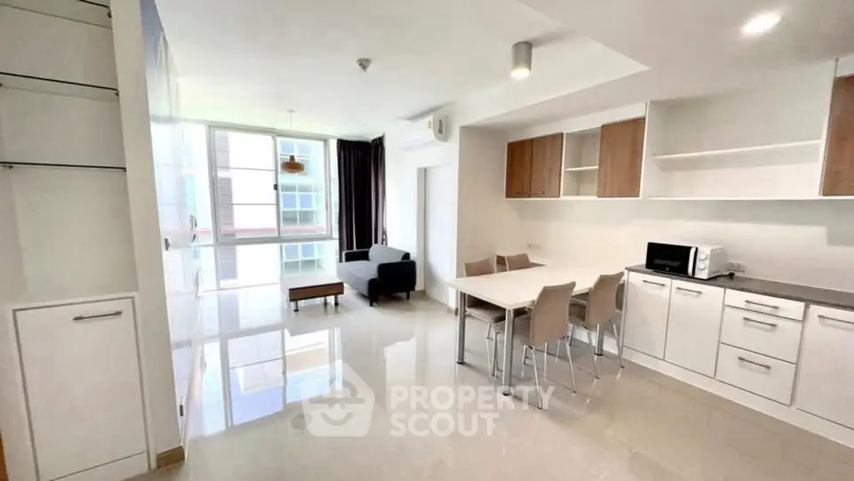 Spacious modern living room with open kitchen and dining area, featuring sleek white cabinetry and natural light.