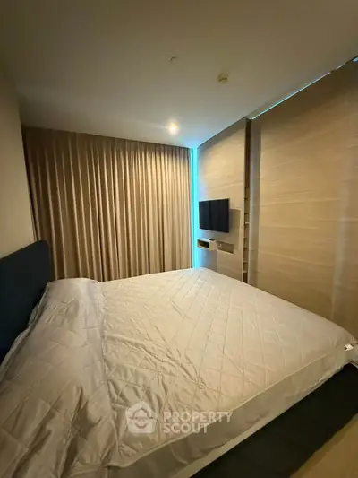 Modern bedroom with sleek design and cozy ambiance, featuring a wall-mounted TV and elegant curtains.