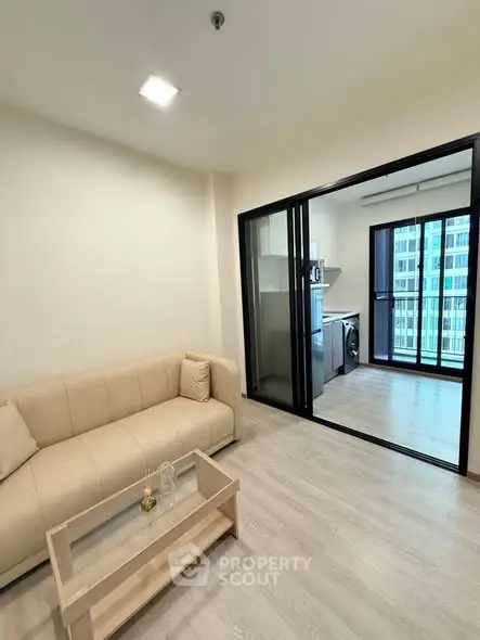 Modern living room with beige sofa and sliding glass doors leading to a balcony with city view.
