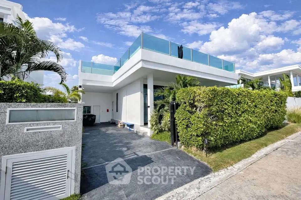 Modern luxury villa with glass balcony and lush greenery under a clear blue sky.