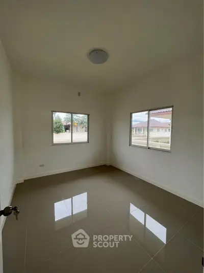 Spacious empty room with large windows and glossy tiled floor in a modern home.